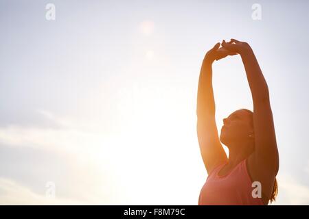 Young female runner stretching armes contre ciel soleil Banque D'Images