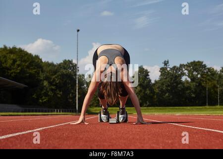 Jeune coureuse avant de flexion sur la race track ligne de départ Banque D'Images