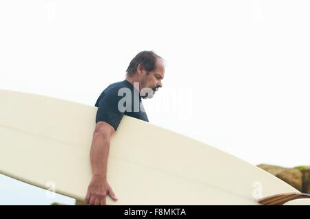 Surfer carrying surfboard Banque D'Images