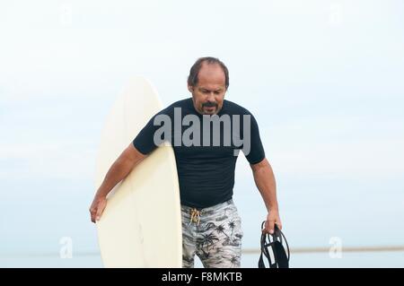Surfer carrying surfboard Banque D'Images