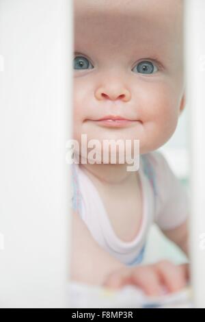 Portrait of baby girl looking through bars sur lit bébé Banque D'Images