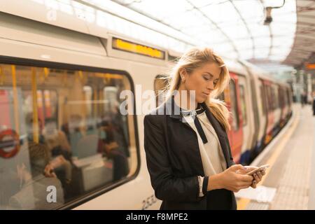 Business Woman texting on plate-forme, station de métro, London, UK Banque D'Images