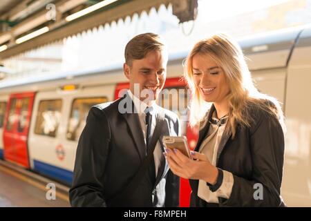 Businessman and businesswoman texting sur la plate-forme, station de métro, London, UK Banque D'Images