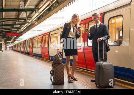 Businessman and businesswoman texting sur la plate-forme, station de métro, London, UK Banque D'Images