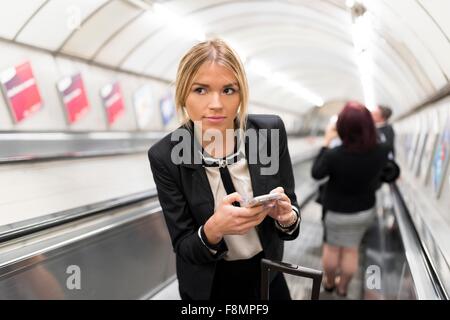Businesswoman texting on escalator, métro de Londres, UK Banque D'Images