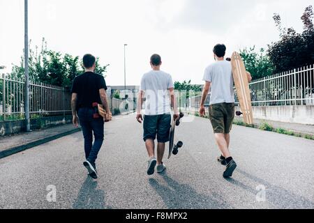 Vue arrière du young men walking on path transportant skateboards Banque D'Images