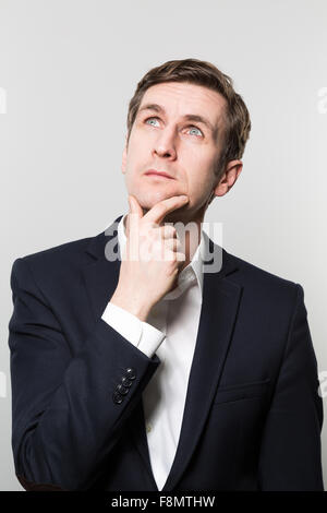 Aux cheveux blonds avec un homme d'oeil pensif regarde le plafond tandis qu'en face d'un gradient background Banque D'Images