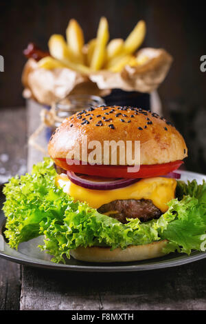 Burger maison avec des graines de sésame noir sur la planche à découper en bois avec pommes frites, avec sauce ketchup dans un bocal en verre Banque D'Images