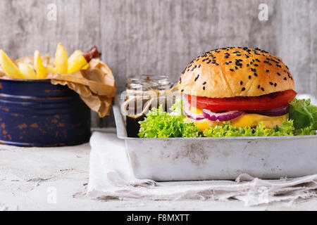 Burger maison avec des graines de sésame noir dans le vieux plateau en aluminium avec des pommes de terre, servi avec sauce ketchup dans un bocal en verre Banque D'Images