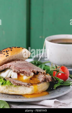 Close up of sandwich fait maison avec de la viande cuit à la coque et d'œuf liquide des oeufs, salade, tomates cerises et tasse de poc Banque D'Images