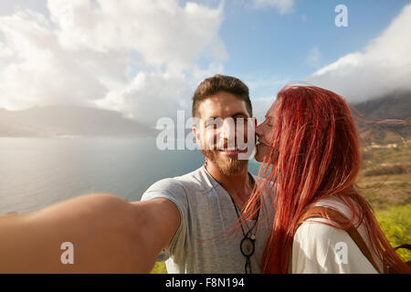 Un couple à l'extérieur. selfies POV shot homme tenant un appareil photo et prendre un autoportrait avec femme l'embrassant. Banque D'Images