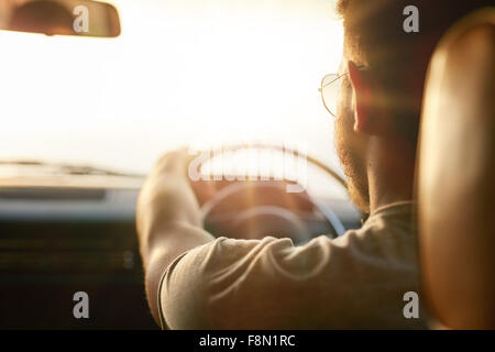 Close up shot of young man driving car. Vue arrière de l'homme sur la route un jour d'été, avec sun flare. Banque D'Images