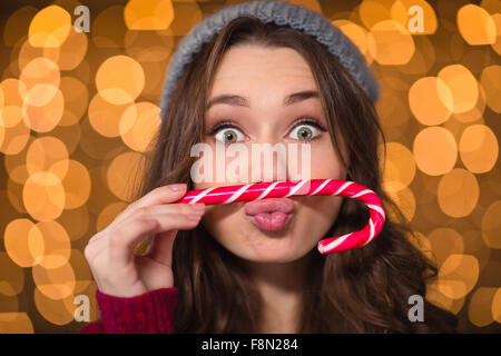 Cute girl making curly amusant drôle de visage à l'aide de canne de Noël sur fond scintillant Banque D'Images