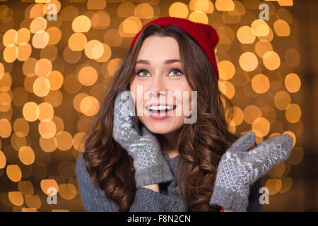 Portrait de belle jeune femme gaie dans Red Hat et mitaines tricotées talking on mobile phone sur fond pétillant Banque D'Images