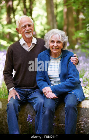 Senior Couple Sitting on Log en bois Bluebell Banque D'Images