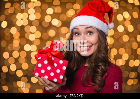 Jeune femme positive amusante à santa claus hat holding présente sur un fond lumineux Banque D'Images