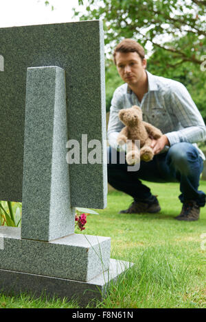 Père plaçant ours sur la tombe de l'enfant dans Cemetery Banque D'Images