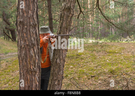 Objectif chasseur Senior carabine debout entre les pins en forêt Banque D'Images