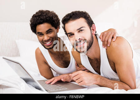 Happy gay couple laying on bed using laptop Banque D'Images