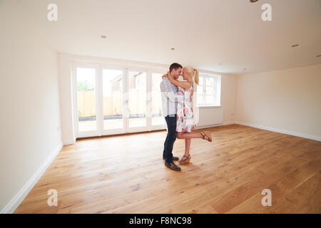 Jeune couple excité en salle vide de leur première maison Banque D'Images