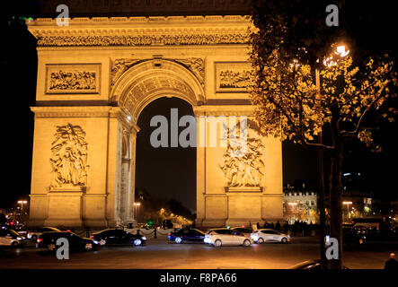 Les voitures roulent autour de la base de l'Arc de Triomphe de nuit à Paris, France Banque D'Images