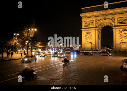 Les voitures roulent autour de la base de l'Arc de Triomphe de nuit à Paris, France Banque D'Images