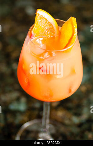 Close-up d'un verre rempli de vin misty dégradé orange liquide opaque et des cubes de glace, décoré de deux des quartiers d'orange, sur un b Banque D'Images