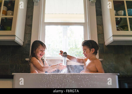 Jeune garçon et fille assise à jouer avec de l'eau d'évier de cuisine Banque D'Images