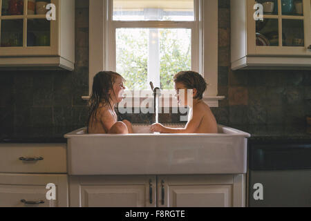 Jeune garçon et fille assise à jouer avec de l'eau d'évier de cuisine