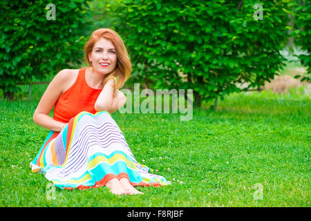 Femme dans une robe est assis sur une pelouse verte Banque D'Images