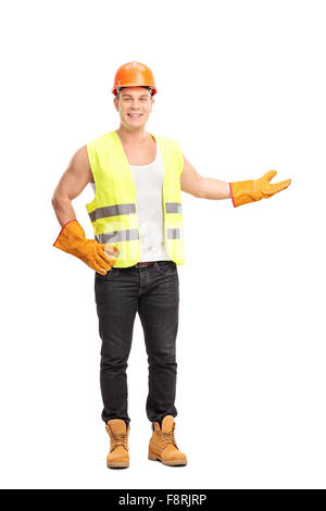 Full Length portrait of a cheerful young construction worker gesturing avec sa main et regardant la caméra Banque D'Images