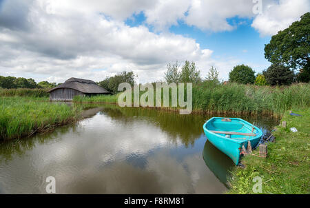 Un aviron turquoise bateau amarré à l'extérieur d'un hangar à chaume traditionnel sur le large Hickling Norfolk Broads Banque D'Images