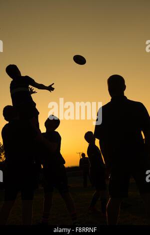 Des silhouettes d'hommes chez les jeunes garçons qui prennent part à la formation pratique de l'entraînement de rugby balle de traitement de l'alignement, à la brunante, Aberaeron Wales UK Banque D'Images