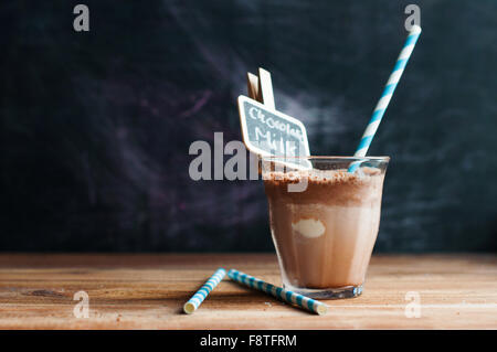 Chocolat chaud avec mousse de lait sur un fond de bois avec du papier de paille, tableau noir avec clip écrit le lait au chocolat Banque D'Images