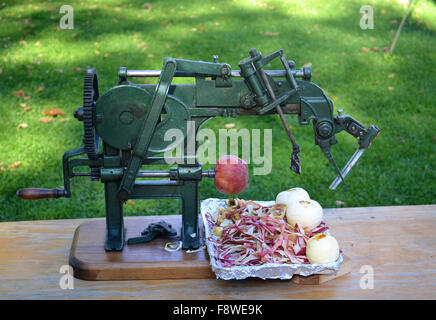 Une très vieille et antique peeler apple assis sur une table avec trois pommes pelées et un en travaux publics. Banque D'Images