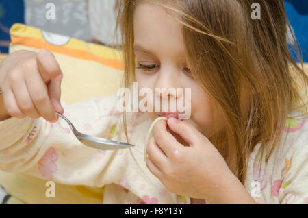 Cheerful fille de cinq ans s'assoit sur le lit et se fait un plaisir de manger les spaghettis Banque D'Images