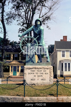 La statue en bronze d'un pêcheur au gouvernail regarde vers le port de Gloucester, Massachusetts, USA, en mémoire des milliers de pêcheurs perdus en mer pendant les trois premiers siècles (1623-1923) de cette nouvelle Angleterre'histoire de la ville. Tiré d'un psaume biblique est le monument bien connu de l'inscription : "ceux qui descendent sur la mer dans des navires.' Il est ciselé sur un grand bloc de granit qui détient les 8 pieds de haut (2.4 mètres) statue par le sculpteur anglais Leonard Craske. Ce célèbre monument est sur le Registre National des Endroits Historiques. Banque D'Images