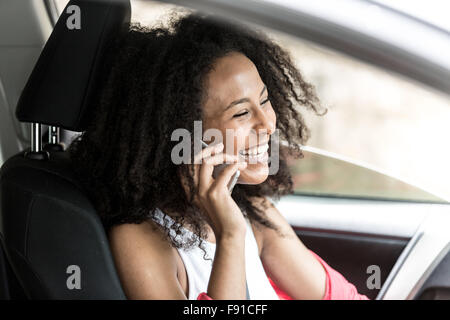 Une jolie jeune femme métisse dans une voiture sur son téléphone mobile comme un passager Banque D'Images