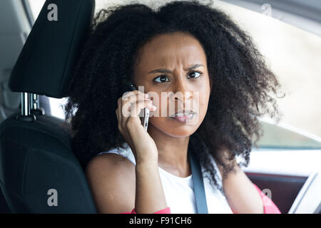 Une jolie jeune femme métisse dans une voiture sur son téléphone portable à la traverser les yeux et fou Banque D'Images