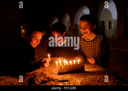 Jeune garçon juif religieux allume une bougie sur une menorah sur le 8e jour de la fête juive de Hanoukka, la fête des lumières, dans Batei Mahseh Square dans le quartier juif de la vieille ville de Jérusalem-Est Israël Banque D'Images