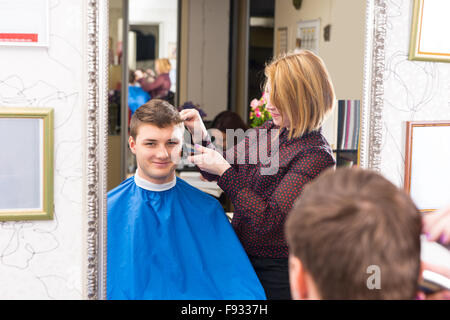 Reflet dans le miroir de Smiling Young Man Having Hair Cut et décoré par blonde styliste en coiffure Banque D'Images