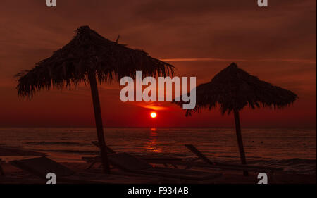 Coucher du soleil à la plage avec des parapluies et quelques chaises au premier plan, le coucher de soleil dans la distance Banque D'Images
