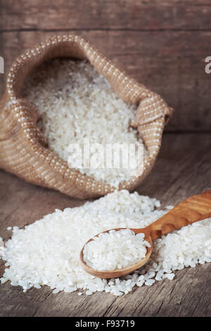 Riz blanc sur la cuillère en bois et dans le sac sac sur le vieux fond de bois Banque D'Images