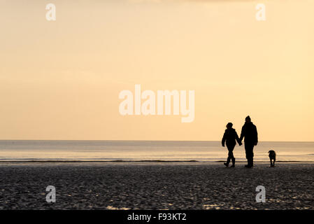 Un couple en train de marcher leur chien et tenir la main sur la plage de Camber, East Sussex. Banque D'Images