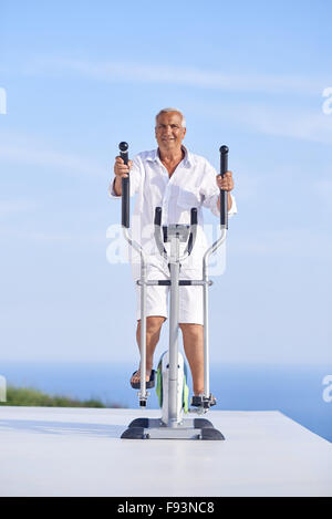 Healthy Senior homme travaillant sur le tapis de la machine à la terrasse d'accueil moderne avec vue sur l'océan Banque D'Images