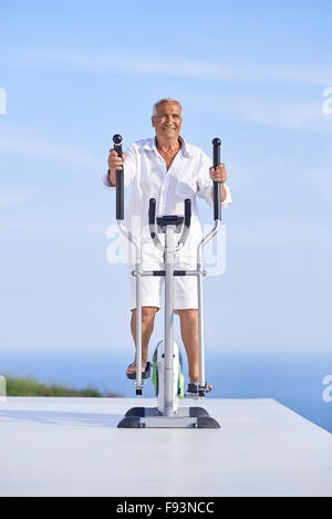 Healthy Senior homme travaillant sur le tapis de la machine à la terrasse d'accueil moderne avec vue sur l'océan Banque D'Images