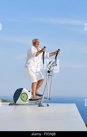 Healthy Senior homme travaillant sur le tapis de la machine à la terrasse d'accueil moderne avec vue sur l'océan Banque D'Images