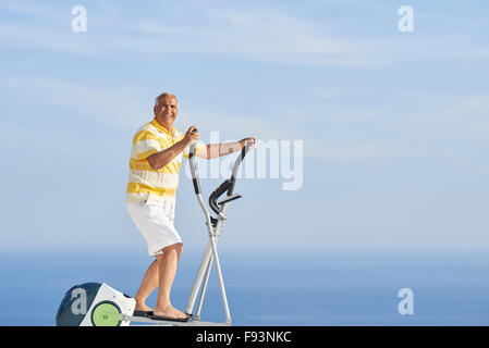Healthy Senior homme travaillant sur le tapis de la machine à la terrasse d'accueil moderne avec vue sur l'océan Banque D'Images