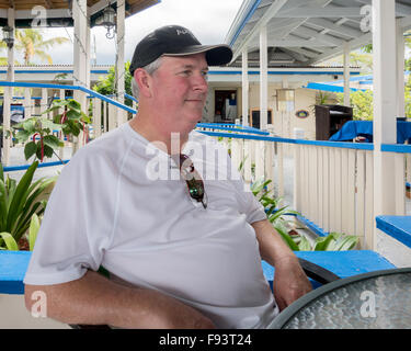 Un homme caucasien de 50 ans en surpoids assis à une table en plein air dans un café en bord de mer à St. Croix, États-Unis Îles Vierges. Banque D'Images