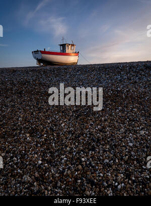 Un seul bateau de pêche attrape la dernière lumière sur la vaste étendue de galets à Dungeness, Kent. Banque D'Images